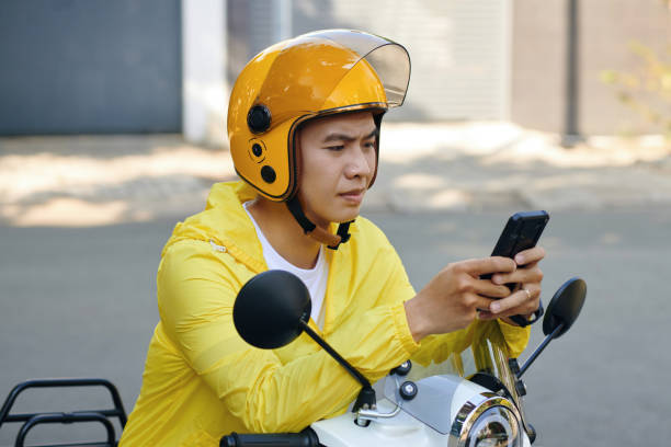Motorbike Taxi Driver Checking Requests Frowning motorbike taxi driver checking request notifications on smartphone vietnamese man taxi motorbike driver stock pictures, royalty-free photos & images