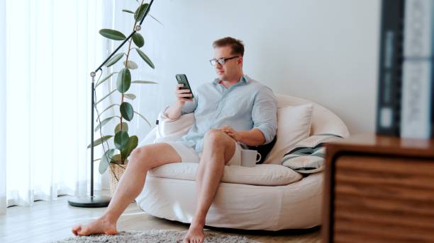 istock Smart man sit on sofa in living room use phone searching for data. Divergence. 2154954330