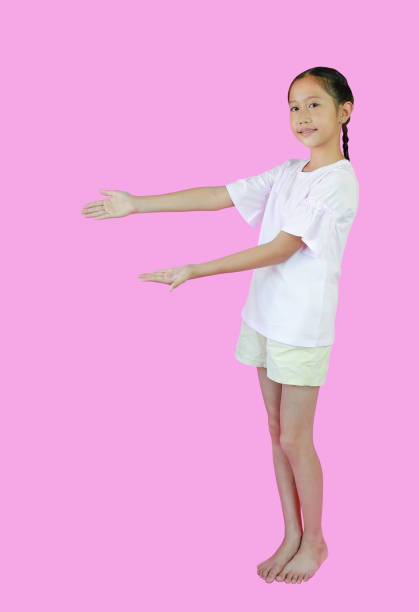 Smiling Asian girl child standing presenting something on copy space, isolated on pink studio background. Image full length with clipping path.