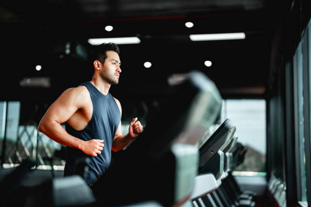 young asian man running on treadmill - fitness gym exercise - fitnesseinrichtung stock-fotos und bilder