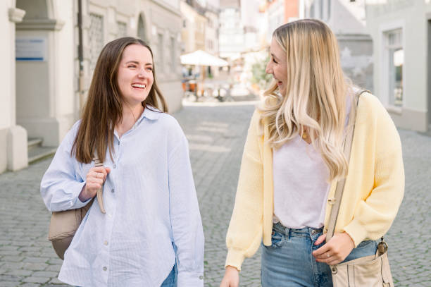 istock female friends talking and laughing while walking along a city 2154960525