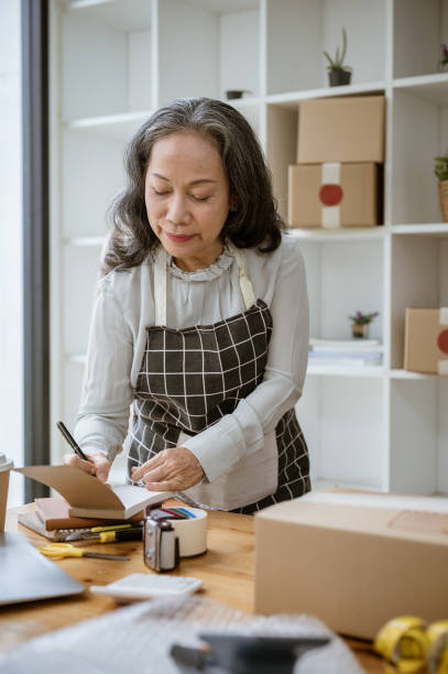 istock A mature Asian female tailor is taking notes on a notepad, measuring and adjusting the pattern. 2154968228