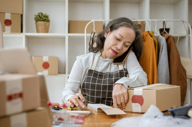 istock A mature Asian female tailor is taking notes on a notepad and receiving orders from the call. 2154968314