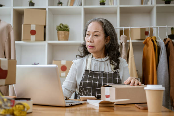 istock A mature Asian female clothes online seller is checking orders from customers on her computer. 2154968324