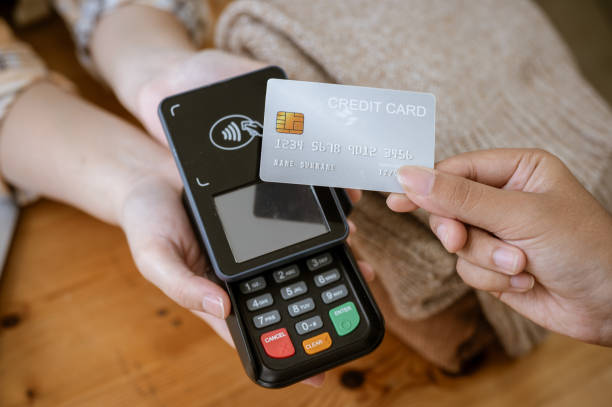 A close-up image of a customer tapping her credit card with a payment terminal in a clothing store. A close-up image of a customer tapping her credit card with a payment terminal or credit card machine at a cashier in a clothing store. cashless payment, card reader, electronic funds transfer clothing store credit card stock pictures, royalty-free photos & images
