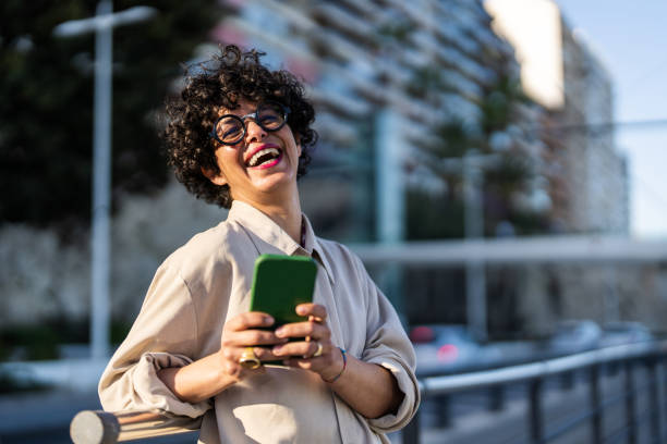 istock Smiling Woman Engaging with Smartphone in Urban Setting 2154971633