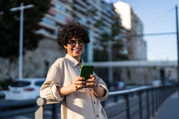 istock Caucasian Woman with Joyful Expression Texting on Smartphone Outdoors 2154971659