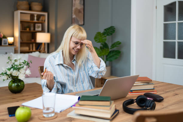 istock Self improvement. Young satisfied student or business woman, working on laptop computer from home, learning from books, to implement innovations in business or study for educational exam. 2154971978