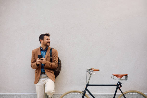 istock Happy businessman texting on mobile phone while leaning on a wall next to his bicycle. 2154984557