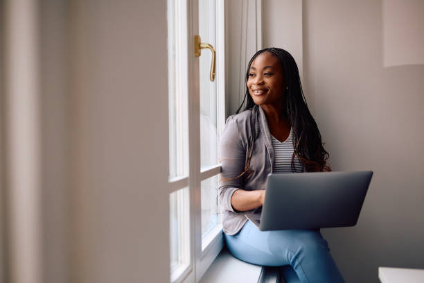 istock Happy black businesswoman using laptop while looking through the office window. 2154984609