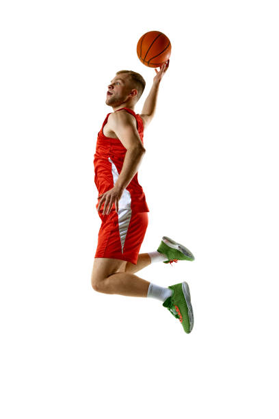 istock Athletic man, basketball player in red uniform jumping in mid-air, performing dynamic slam dunk against white studio background. 2154988862
