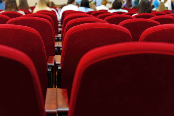 Rows of red velvet chairs in a hall with distant figures