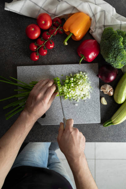 Man hands cutting green onions on chopping board at home