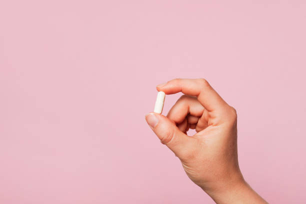 istock Woman hand holding a white pill against a plain pink background, copy space 2154990164