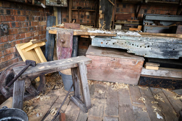 Oblique view of assorted antique wooden hand planes mounted on weathered white barn wall, showing rich patina, threaded clamp screws and rustic roof detail in traditional carpentry workshop