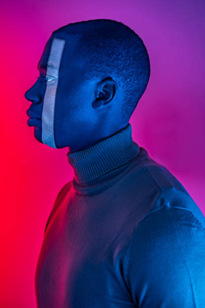 A side profile view of an African-American man with a vertical band of white light down one side of his face, wearing a turtleneck sweater against a gradient red to purple background