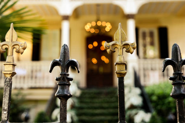 A cast wrought iron fence lined with black and gold fleur de lis post toppers with a New Orleans southern style home in the background A cast wrought iron fence lined with black and gold fleur de lis post toppers with a New Orleans southern style home in the background. new orleans fleur de lis stock pictures, royalty-free photos & images