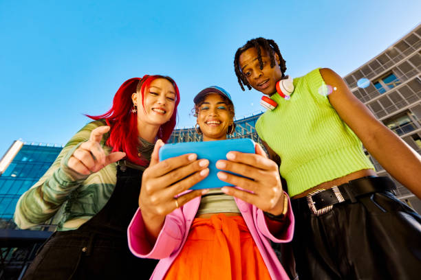 istock Three Gen Z friends using a smartphone together. Low angle shot with modern buildings in the background. Social media and friendship concept. 2155004312