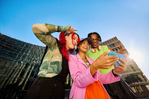 istock Three Gen Z friends using a smartphone together. Low angle shot with modern buildings in the background. Social media and friendship concept. 2155004313