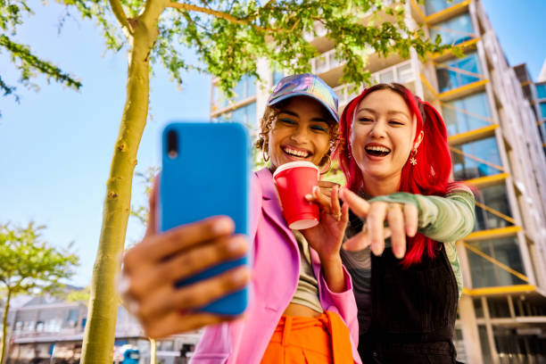 istock Two Gen Z adults using a smartphone and holding a drink outdoors in an urban environment. Low angle shot. 2155004357