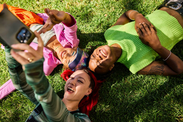 istock Three Gen Z adults lying on grass and taking a selfie outdoors in a park. Top view. 2155004401