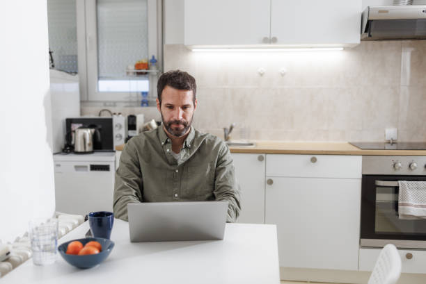 istock Man working remotely on a laptop in a modern kitchen 2155020363