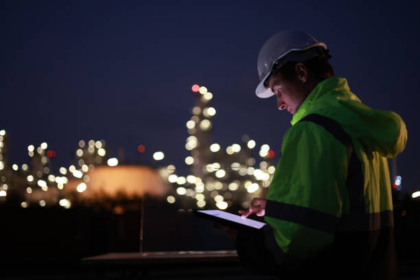 istock A night shift engineer in a hard hat and reflective jacket is focused on a tablet with the illuminated industrial plant in the background. 2155022507