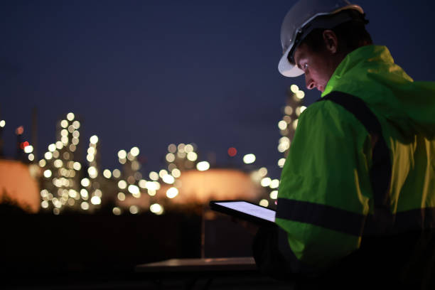 istock A night shift engineer in a hard hat and reflective jacket is focused on a tablet with the illuminated industrial plant in the background. 2155022544