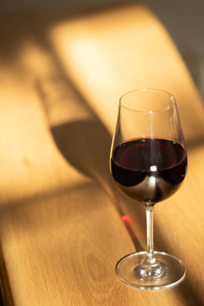 istock Red glass on a table top with hard shadows from a sunlight that passes through a window 2155025871