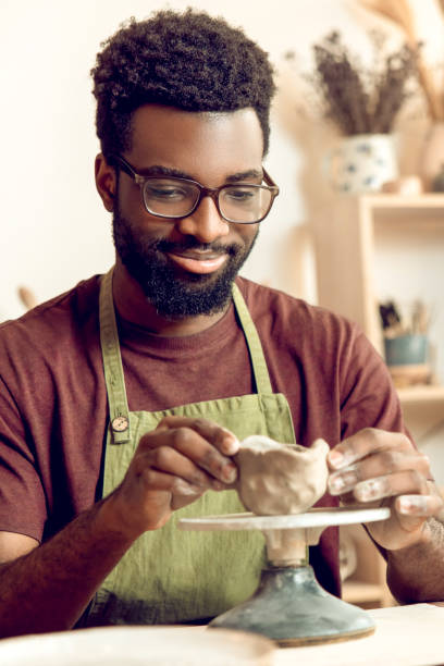 istock Dark-skinned man in eyeglasses shaping mug from clay and looking focused 2155026101