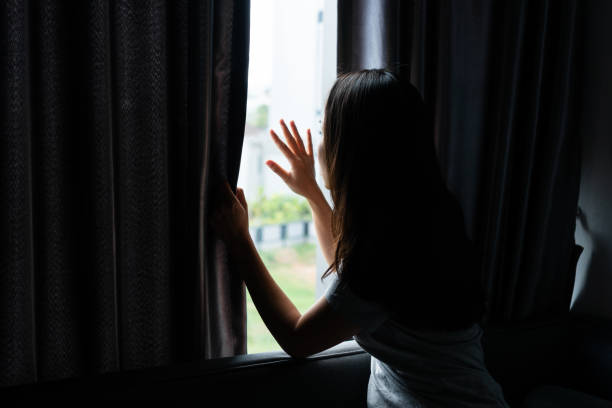 istock Young Asian woman with depression sitting alone on sofa while looking out the window at home. Sad, unhappy, disappointed and lonely concept 2155032092