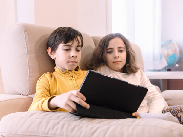 istock Two children are closely sitting on a sofa, engaged with a tablet 2155036341