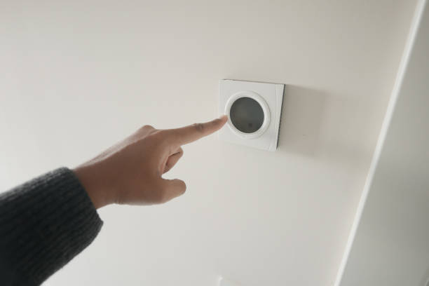 istock Hand Adjusting Smart Thermostat on White Wall for Optimal Home Temperature Control 2155045928