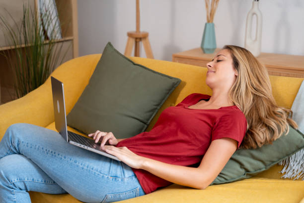 istock Relaxed young woman sitting on a sofa, using her laptop with eyes shut 2155047246