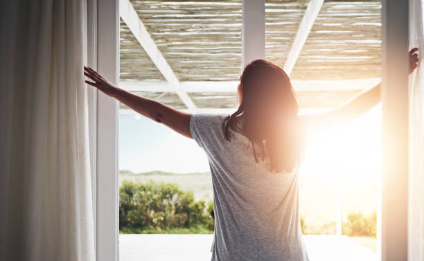 atrás, mujer y cortina abierta por la mañana, ventana y despertar fresco con el amanecer en el hotel listo para el día. rutina, vista exterior y naturaleza en vacaciones o fin de semana, cortinas y luz en apartamento en dormitorio - vista desde la ventana fotografías e imágenes de stock