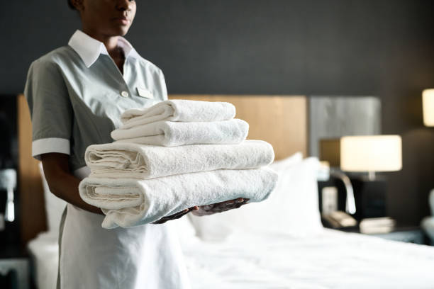 Cropped shot of young African American woman as housekeeper holding stack of fresh bedding preparing room in luxury hotel copy space