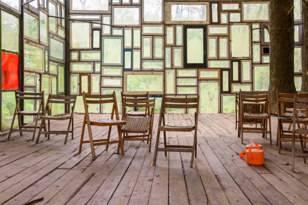 Chairs criss-crossed with small orange elements standing in a glasshouse made with windows