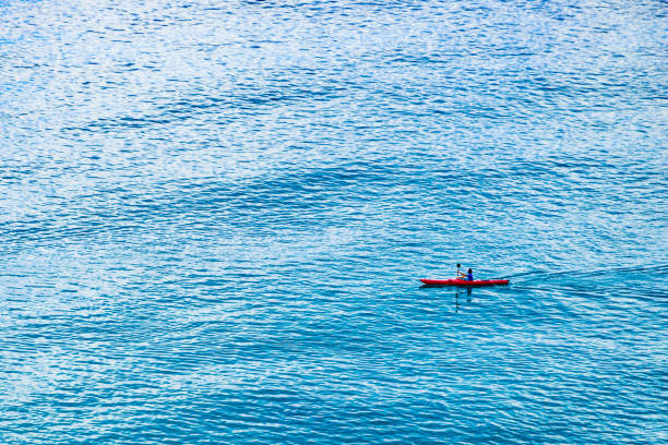 Woman paddles ocean kayak out to sea at sunset