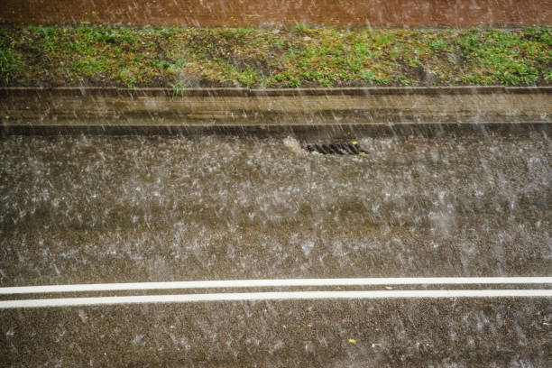 Rain in city. Heavy drops falling on street during downpour. Water flowing to in grate sewer. Sewage system along road. Autumn season