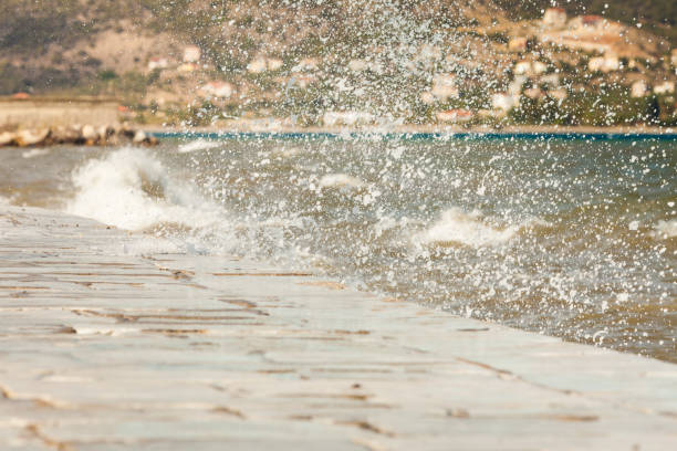 Sea water splashing on the edges of jetty pier reservoir wall in coastline town Greece.