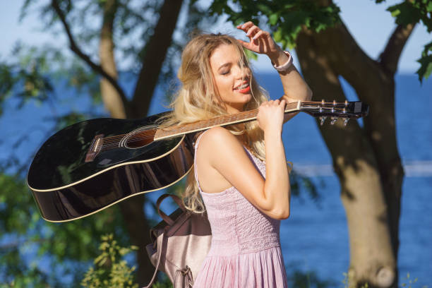Hippie looking young adult woman wearing gypsy outfit having acoustic guitar. Female playing music in park.