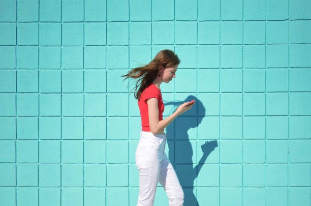 istock Teen girl walking while using a smartphone against a blue wall. 2155088159