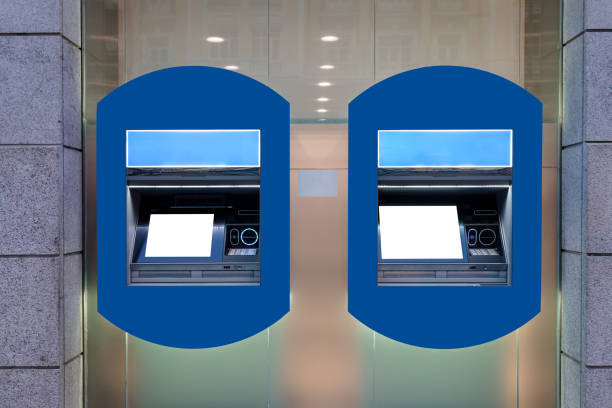 Two blue ATM machines with empty white screens on a wall outside a building