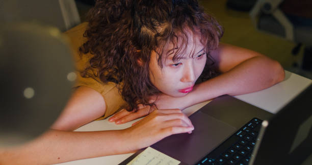 istock Closeup of exhausted young Asian entrepreneur with curly hair facing burnout while working on her laptop late at night in the office. ESG sustainable business office. 2155102811