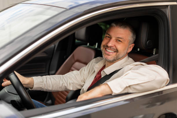 istock Cheerful middle aged man driving auto, looking through open window and smiling at camera, happy driver enjoying car ride 2155104657