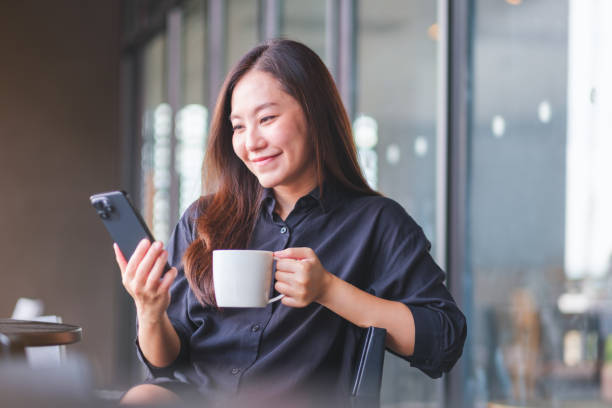 istock Portrait image of a young woman holding and using mobile phone while drinking coffee in cafe 2155115143
