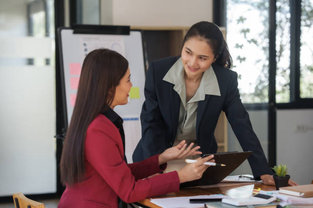 istock Two asian businesswomen discussing and reviewing documents in office. Professional workplace consultation. Corporate business and teamwork concept. 2155116579