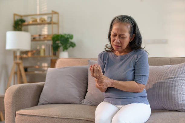 istock Elderly asian woman at home with a pained expression, clutching her hand, possibly dealing with arthritis or injury. 2155117266