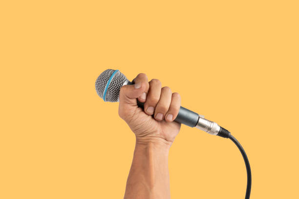 istock Black male hand holding a microphone isolated on yellow background 2155120208