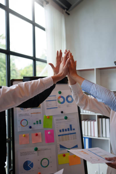 Business team giving a high five in front of a data chart during a successful meeting.